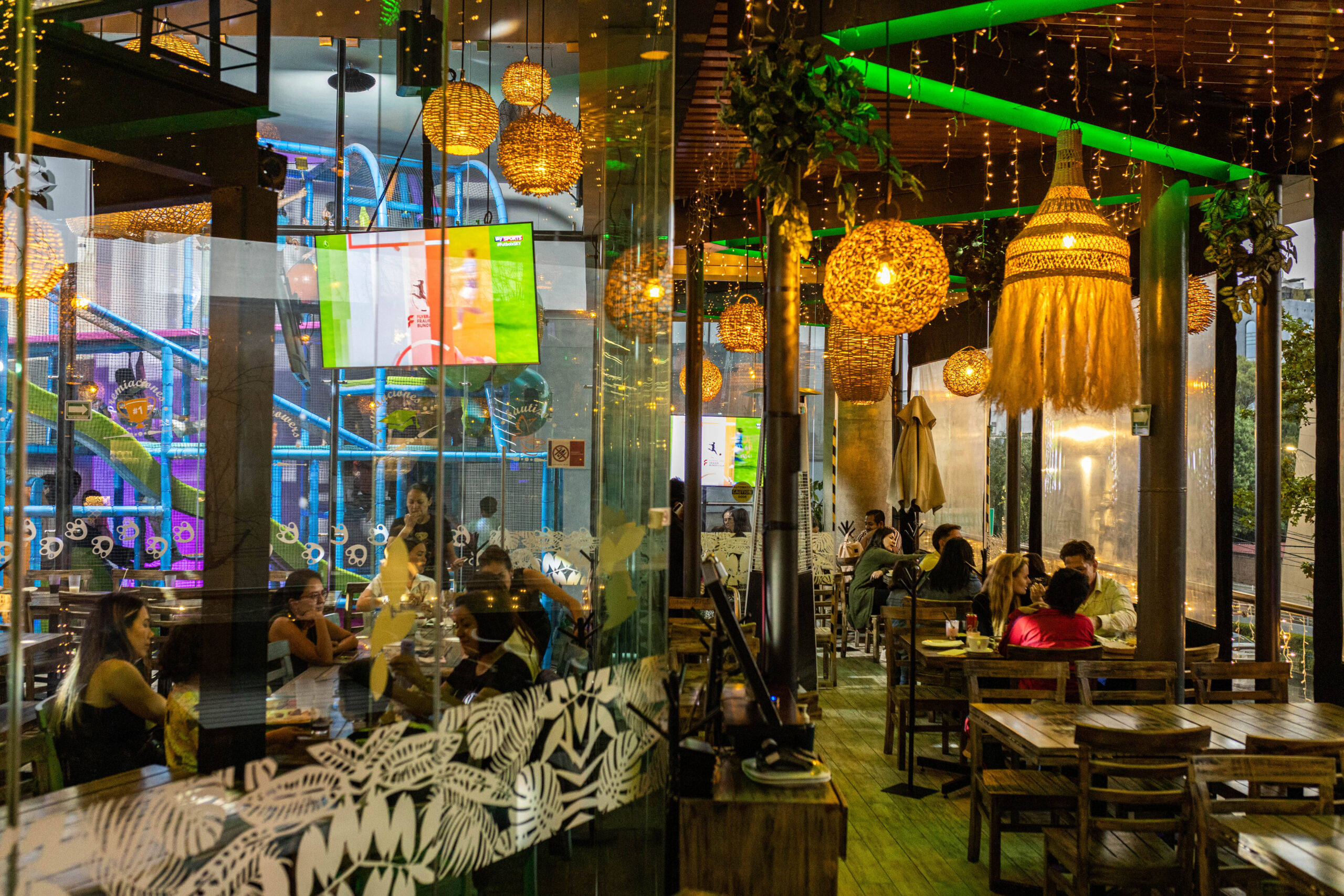 Interior view of a restaurant with decorative lighting and patrons dining at wooden tables.