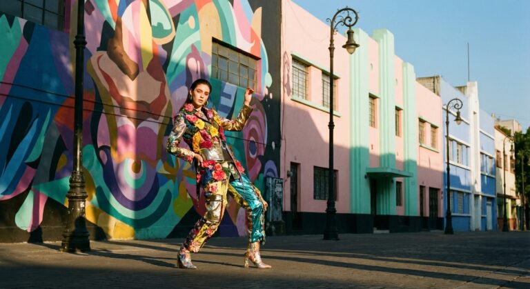 Model posing in a colorful floral outfit against a vibrant mural backdrop in an urban setting.