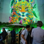 Invitados conversan frente a un mural multicolor de jaguar durante Ledger Leaders Week 2026, con luces verde neón y ambiente de networking en México.