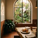 A warm restaurant dining room opens to a lush courtyard, with a rustic wooden table set with plated seasonal dishes in Condesa.
