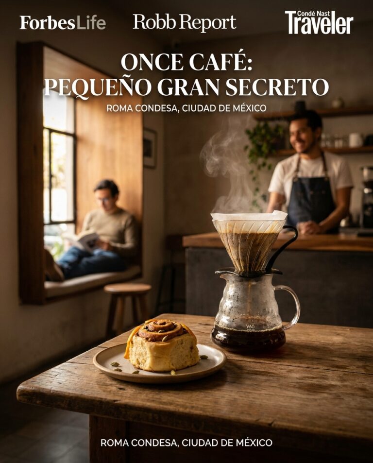 Inside Once Café in Roma Condesa, a steaming pour-over sits beside a cinnamon roll on a wooden table while a barista and reader soften the background.