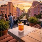 Guests enjoy cocktails on an exclusive Condesa rooftop overlooking tree-lined streets and pink buildings at sunset.