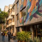 Un mural abstracto de arte urbano cubre la fachada de un edificio en una calle de la Condesa, junto a peatones y un café.
